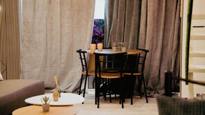 Une pièce chaleureuse avec une table ronde, deux chaises, une petite plante en pot et une fenêtre avec des rideaux.