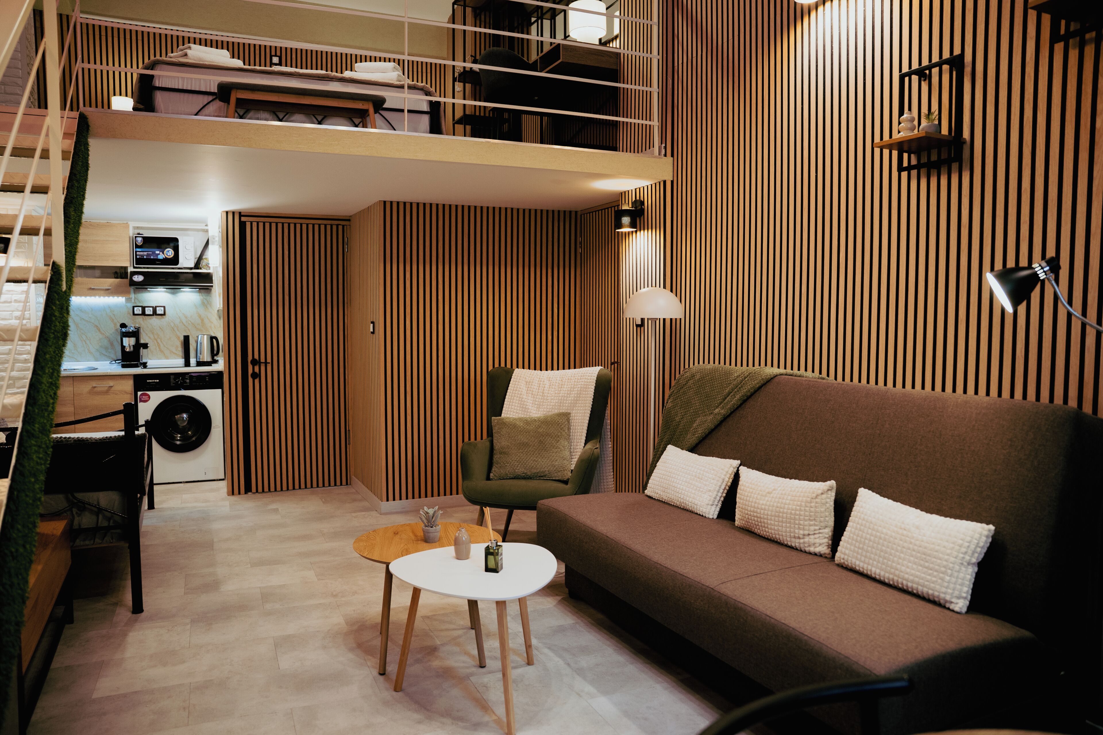 Ein modernes Interieur mit einer Couch, einem Sessel, einem kleinen Tisch, einer Waschmaschine und einer Treppe.