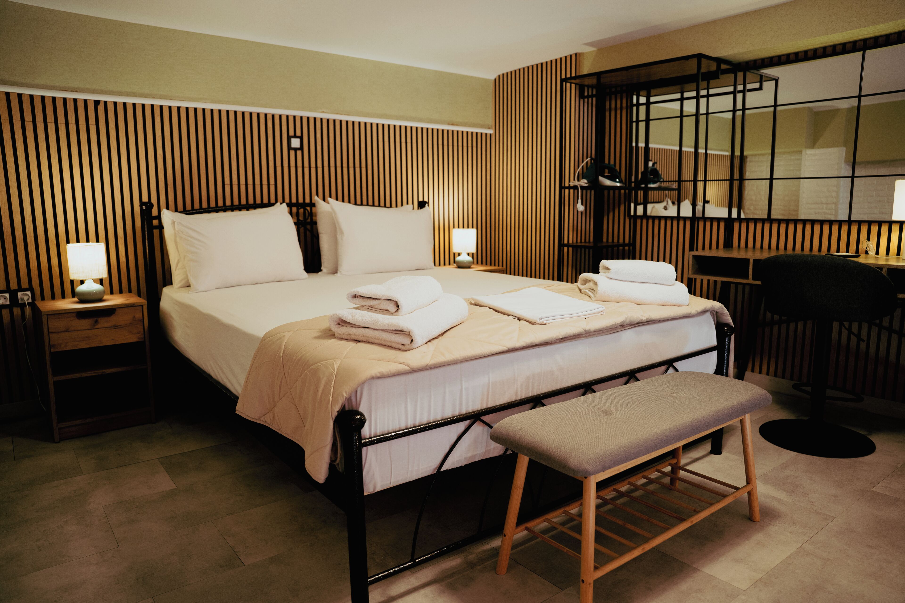Quarto de hotel com cama, mesas de cabeceira, um banco, escrivaninha e espelho.