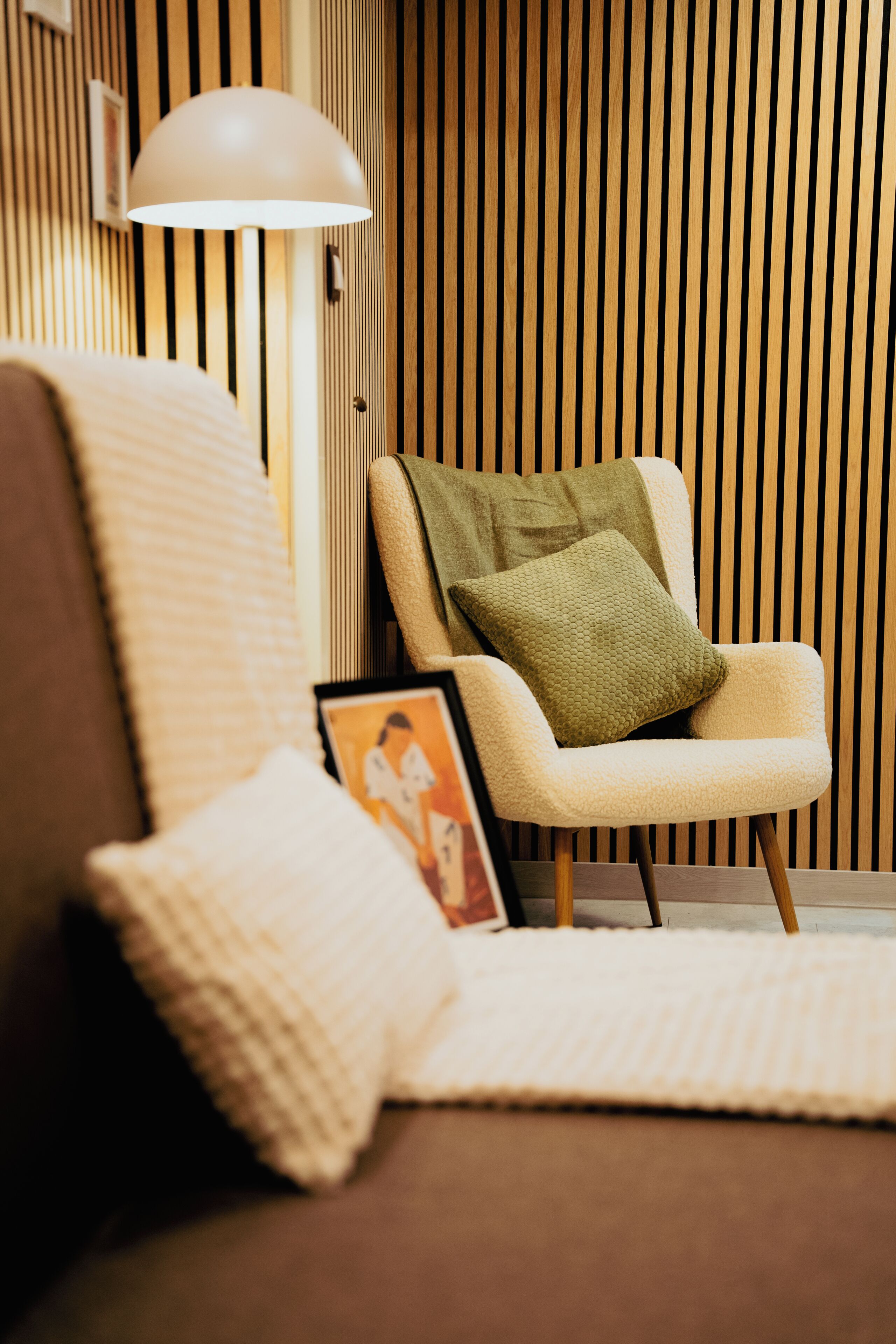 A modern living room with a sofa, a chair with a cushion, a lamp, and a framed picture on the floor.