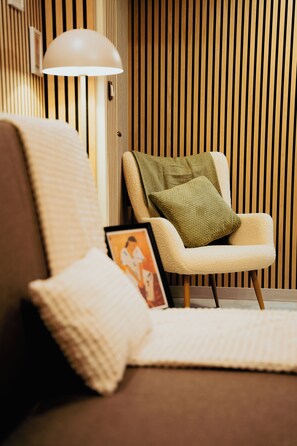 A modern living room with a sofa, a chair with a cushion, a lamp, and a framed picture on the floor. - Koukaki Premium Lofts (Athina)