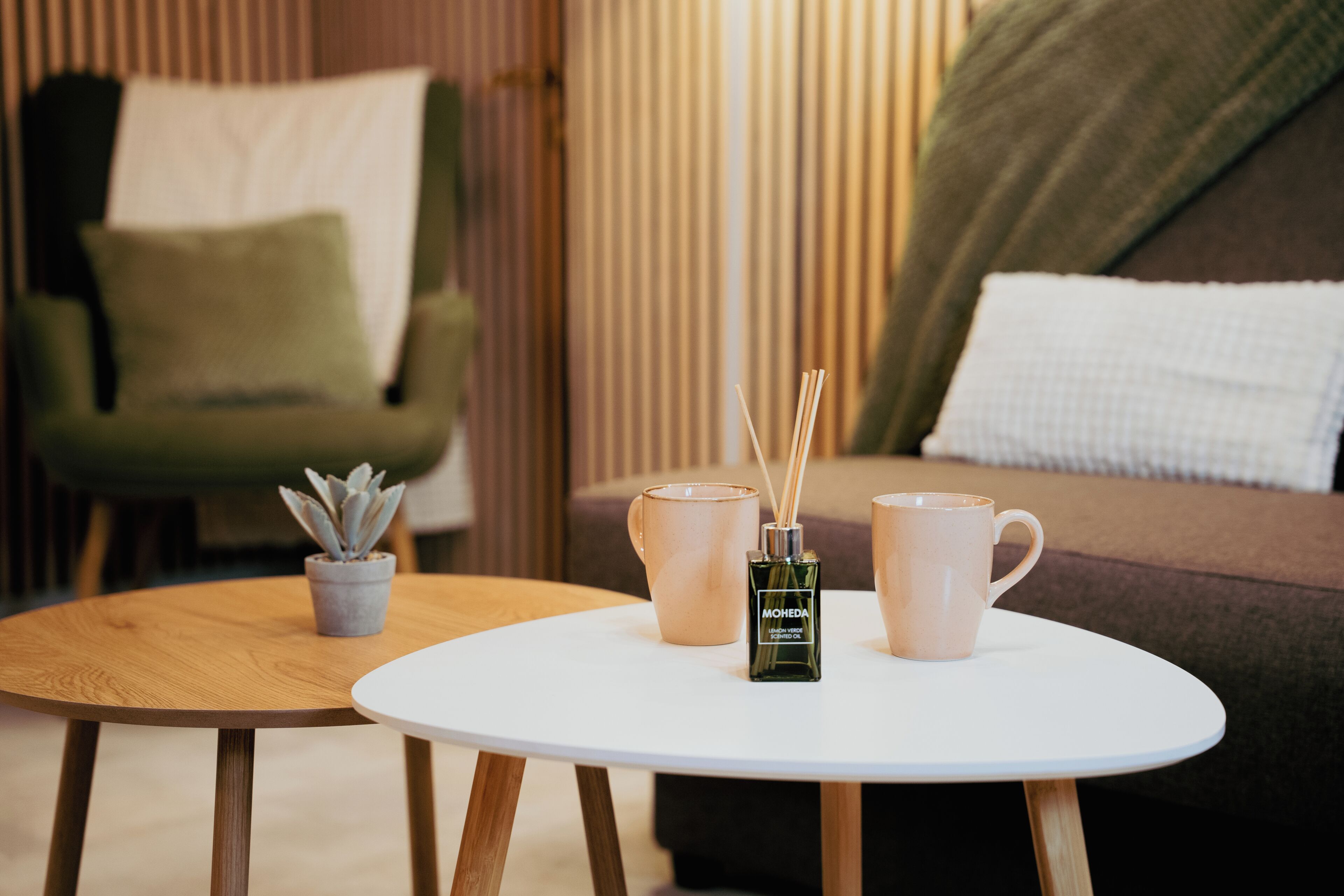 A room with a round wooden table, a potted plant, and two ceramic mugs on the table.