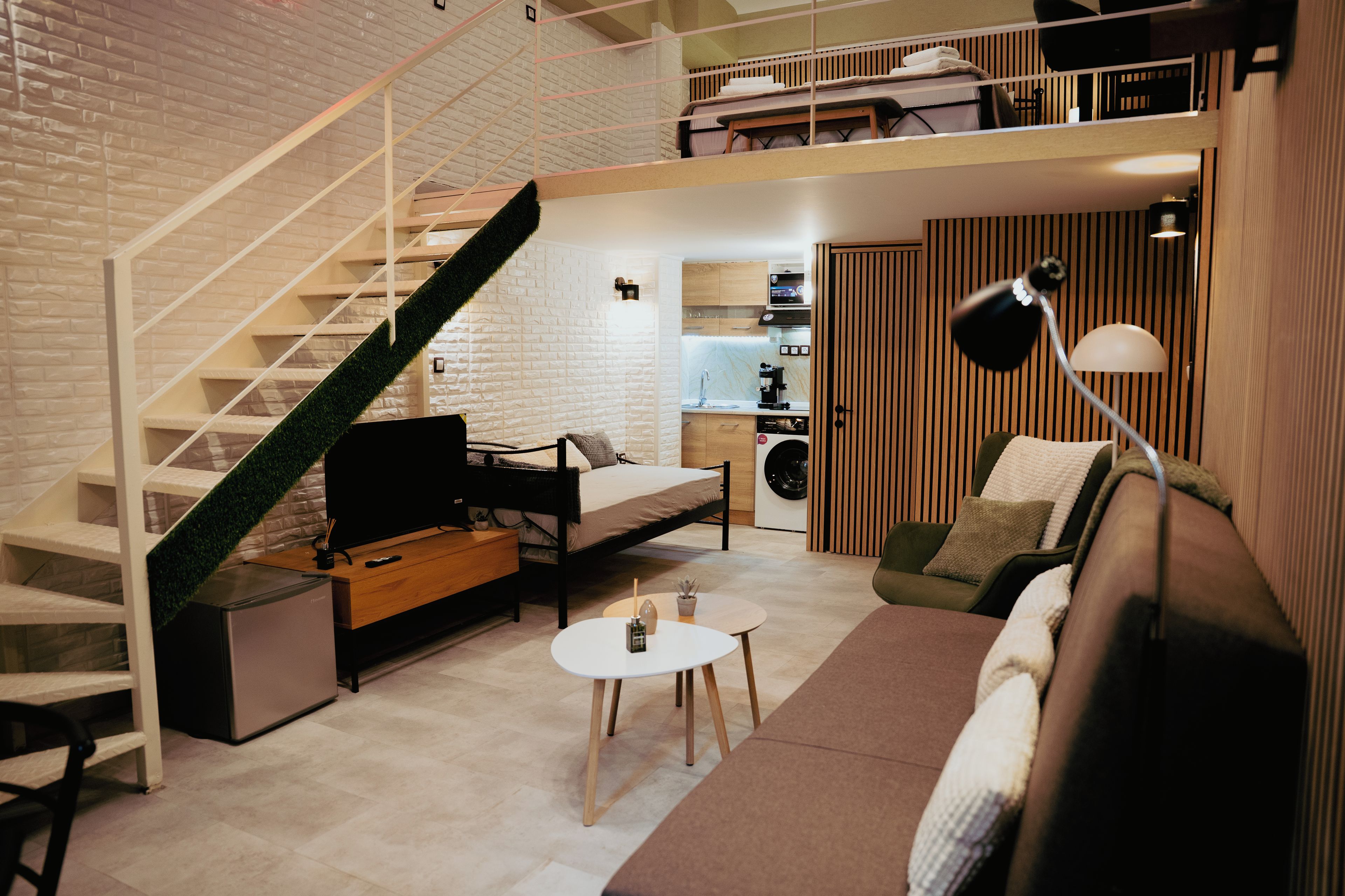 A compact living space with a sofa, a small table, a TV, a staircase, and a kitchen area.