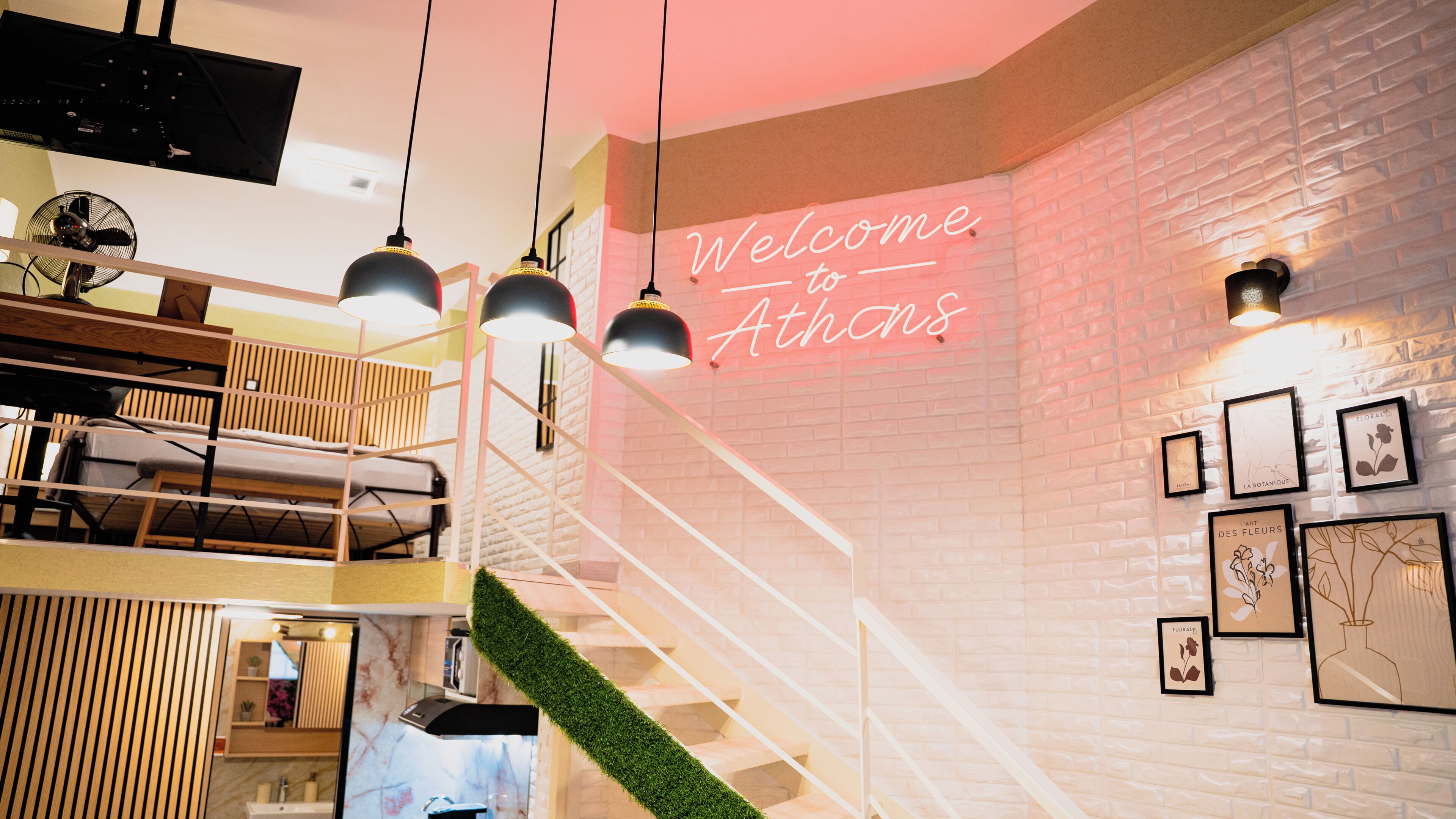A modern interior with a staircase, a neon sign reading 'Welcome to Athens,' and framed botanical artwork on the walls.