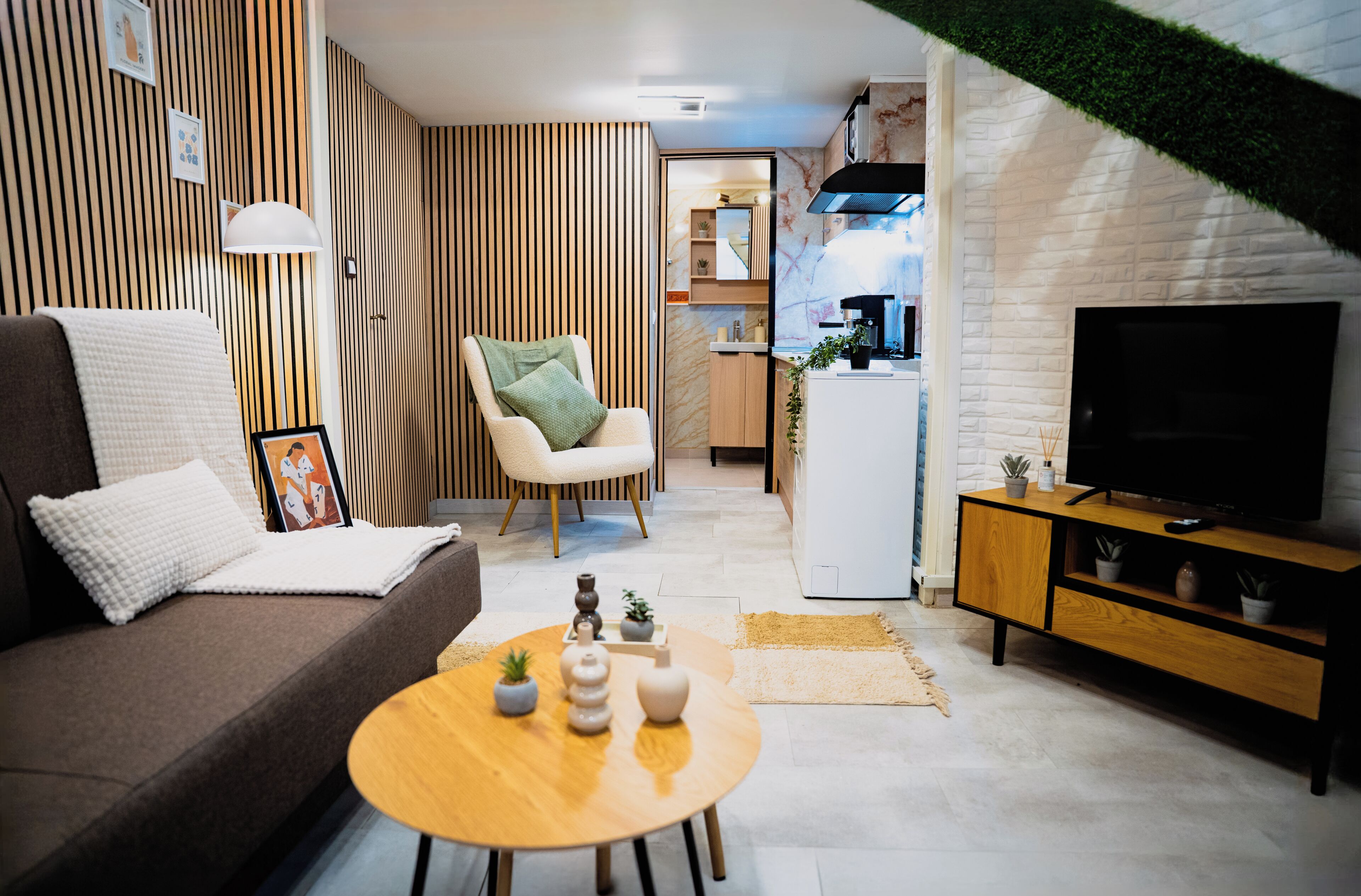 A modern living room with a sofa, a coffee table with decorative items, a television, and a kitchen area in the background.