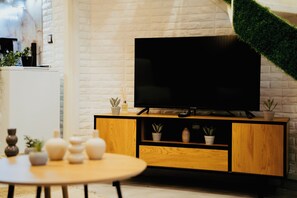 Ein modernes Wohnzimmer mit einem Flachbildfernseher auf einer Holzeinrichtung, einem Esstisch mit Stühlen und einer weißen Ziegelwand.