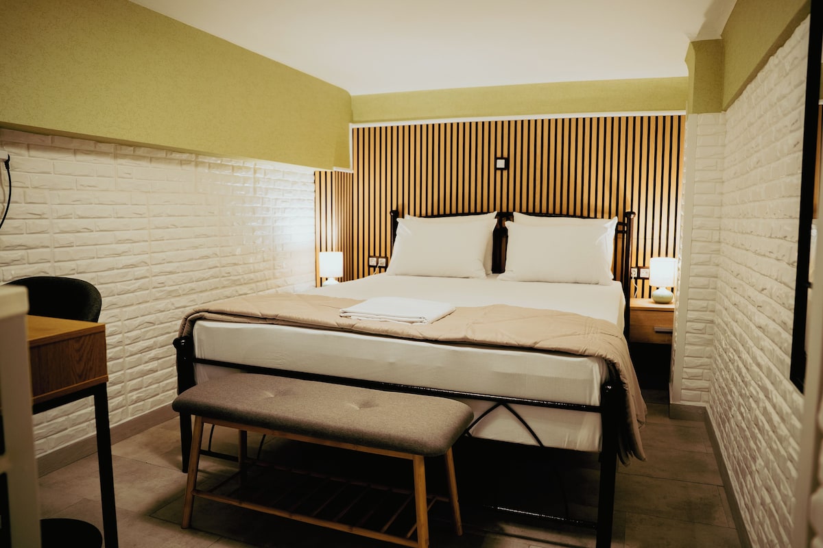 A neatly arranged hotel room with a bed, bedside tables, a bench, and a desk.