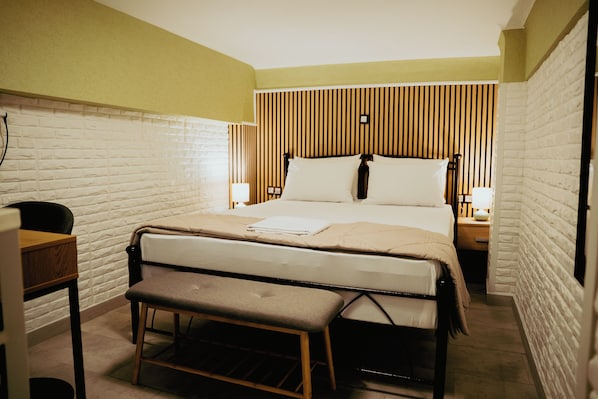 Une chambre d’hôtel bien aménagée, avec un lit, des tables de chevet, un banc et un bureau.