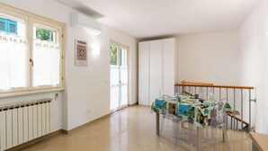 Amplia habitación con una mesa de comedor preparada para cuatro personas, un radiador y una escalera con barandilla de madera.