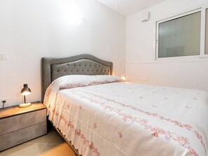 Ein Schlafzimmer mit einem Bett, einem Nachttisch, einer Lampe und einem Fenster.