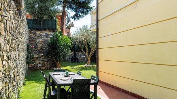 Un patio al aire libre con una mesa y sillas, rodeado por un muro de piedra y vegetación.