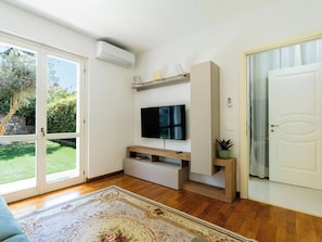 Una sala de estar moderna con una televisión de pantalla plana, mueble de entretenimiento de madera y un ventanal con vistas a zonas verdes.