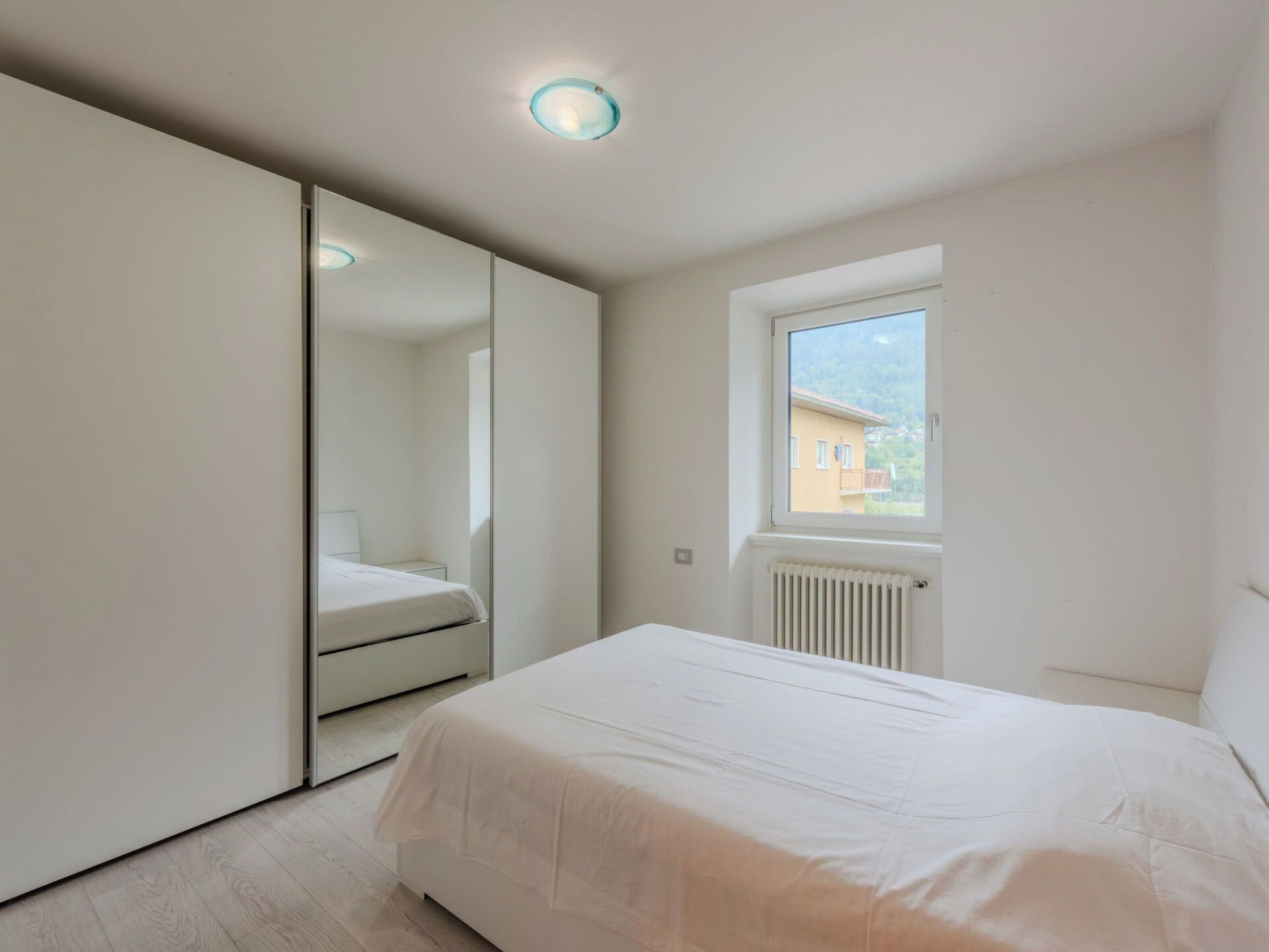 A bedroom with a bed, a window, a radiator, and a mirror.
