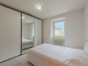 Ein Schlafzimmer mit einem Bett, einem Fenster, einem Heizkörper und einem Spiegel.