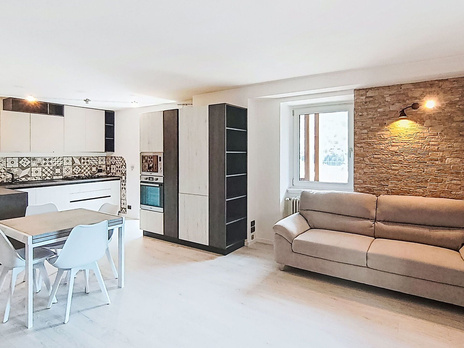 Een moderne keuken met witte kasten, een eettafel met stoelen en een ingebouwde boekenkast.