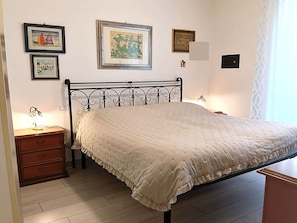 Una camera da letto con un letto, un comodino e una cassettiera. Alle pareti ci sono quadri incorniciati.