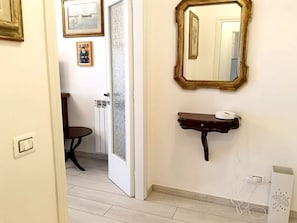 Casa de banho com porta branca, toucador de madeira pequeno, espelho e chão em azulejo.