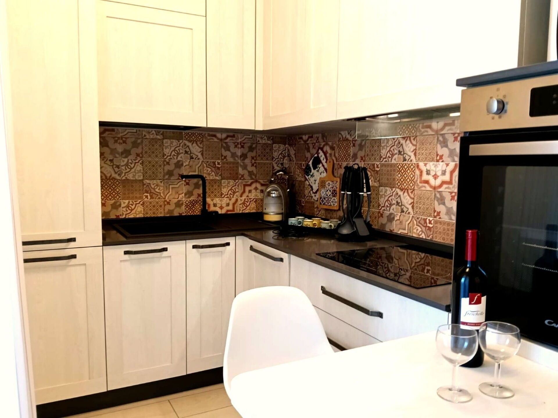 A kitchen with white cabinets, a patterned backsplash, a coffee machine, and a wine bottle on the counter.