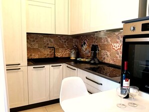 Cozinha com armários brancos, painel decorativo atrás do fogão, cafeteira e uma garrafa de vinho no balcão.