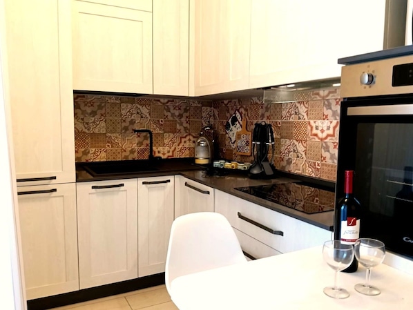 Una cucina con mobili bianchi, uno schienale decorato, una macchina per caffè e una bottiglia di vino sul piano di lavoro.