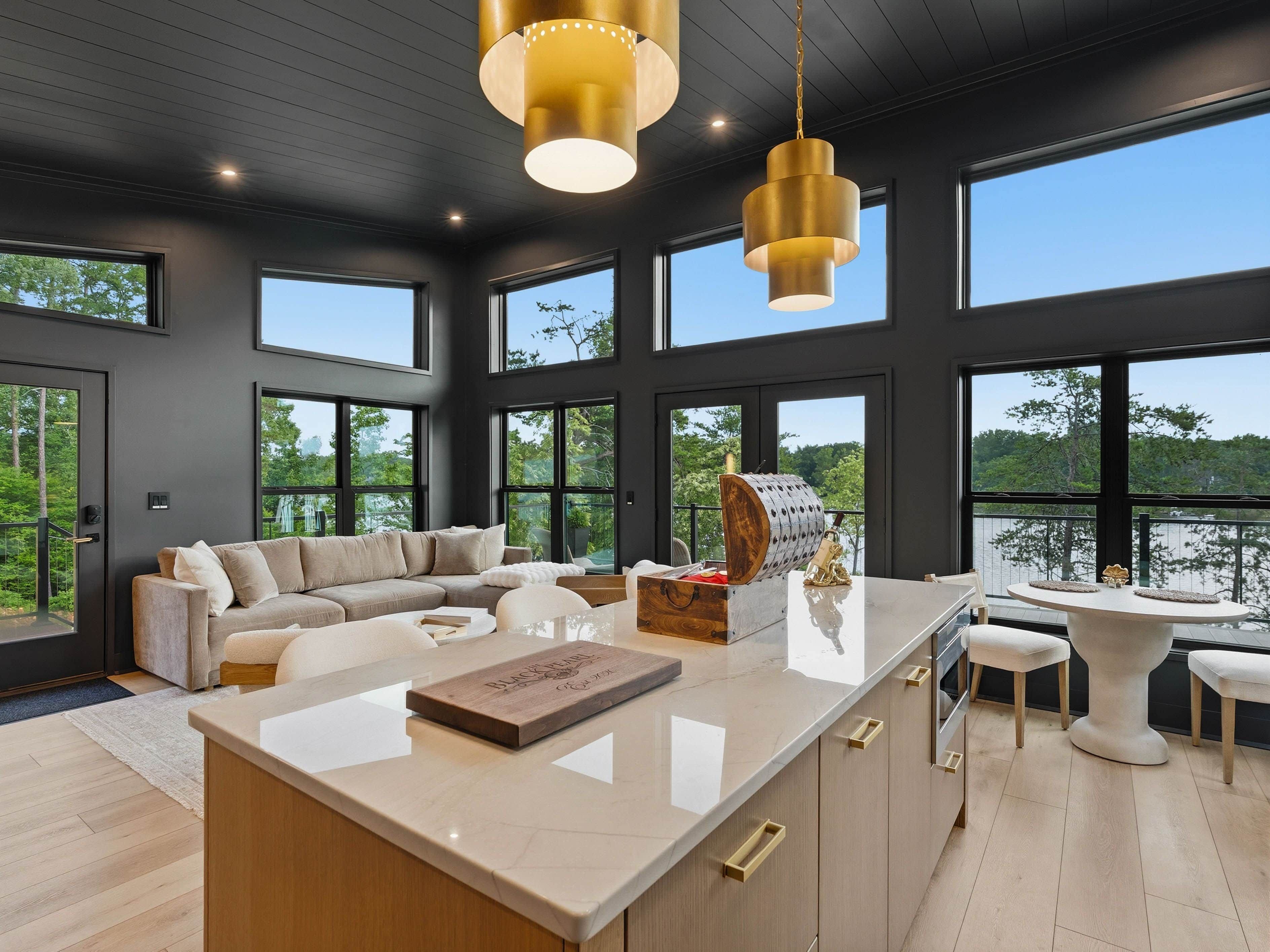 A modern interior with a large central island, dark walls, and large windows offering views of the outdoors.