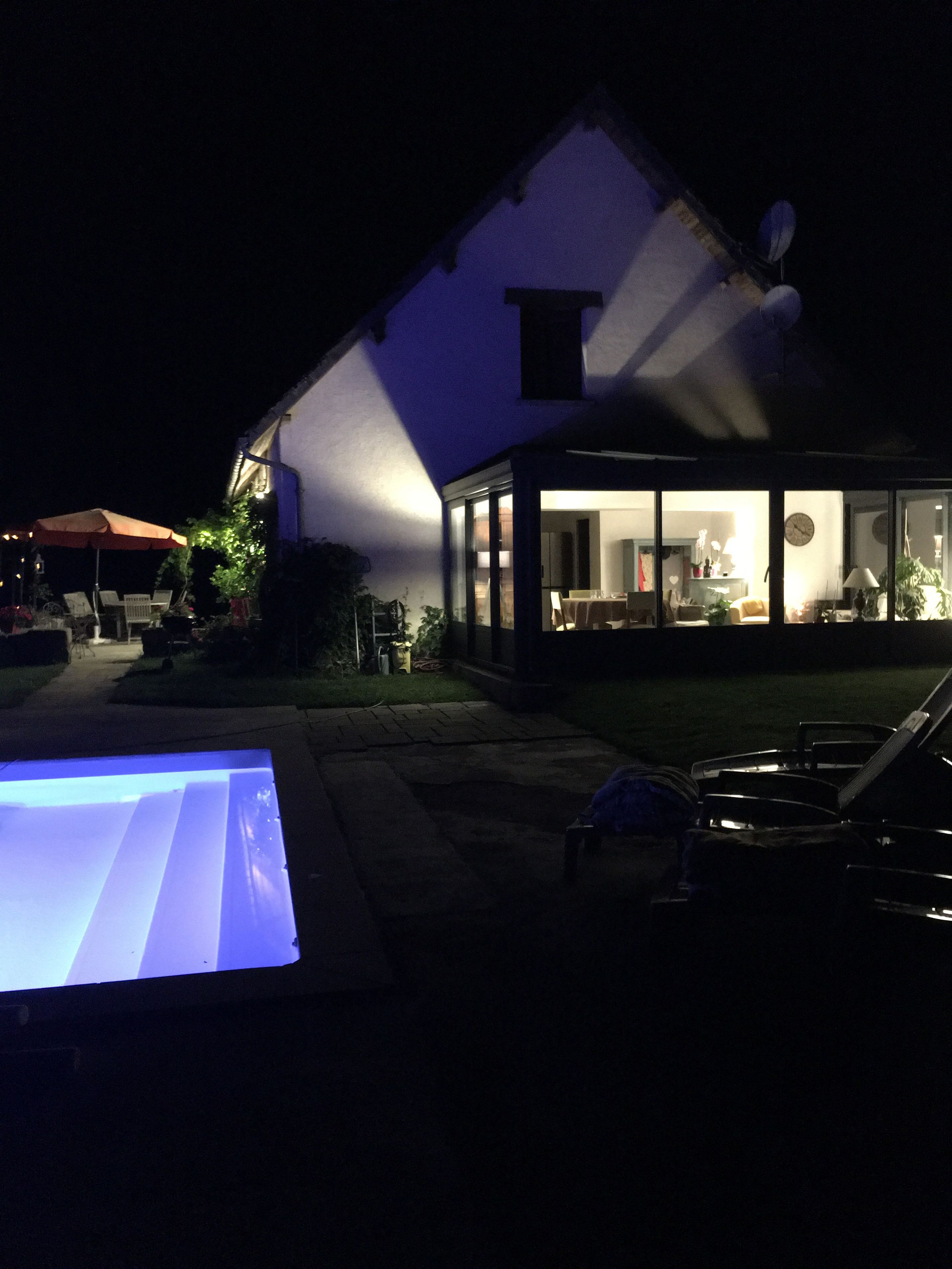 Une maison dotée d’une grande porte vitrée donnant sur un espace intérieur, d’une antenne parabolique sur le toit et d’une pelouse aménagée avec du mobilier d’extérieur.