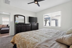 Une chambre à coucher comprenant un lit, une commode, un téléviseur et une fenêtre avec des stores.
