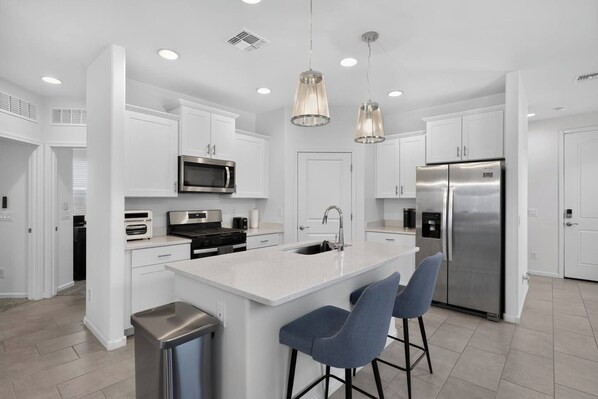 A modern kitchen with white cabinetry, stainless steel appliances, a central island with bar stools, and pendant lighting. - Mins to Banner* St. Mary’s* El Rio* TUS Airport (Tucson)