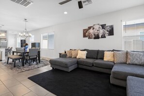 A modern living room with a sectional sofa, a dining area with a chandelier, and a kitchen in the background. - Mins to Banner* St. Mary’s* El Rio* TUS Airport (Tucson)