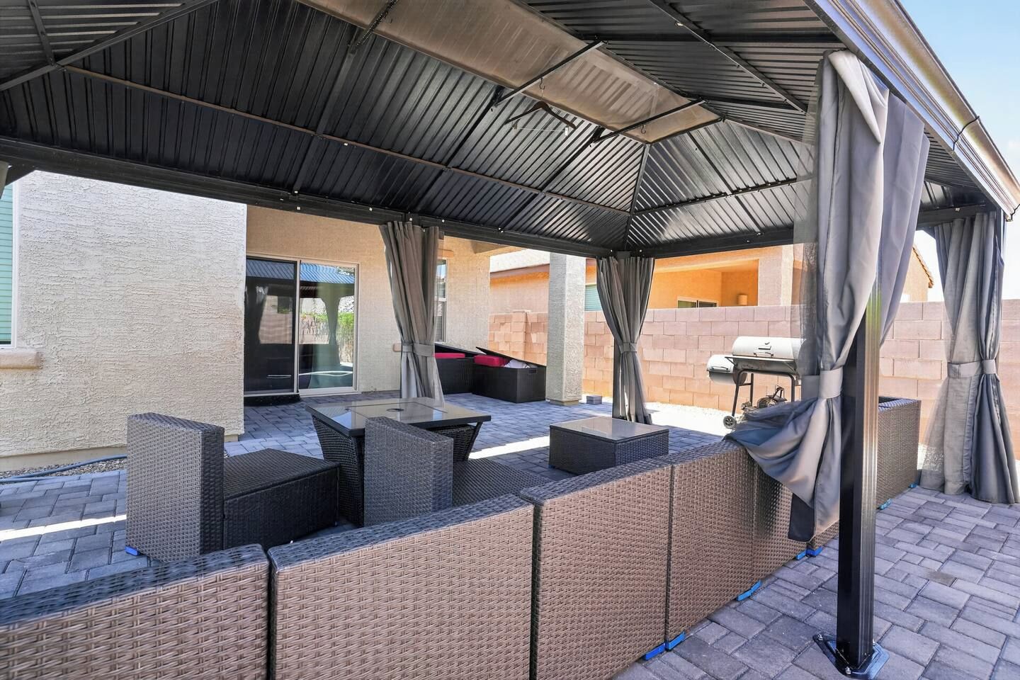 An outdoor patio with a covered seating area, a grill, and a view of the house.