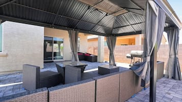 An outdoor patio with a covered seating area, a grill, and a view of the house.