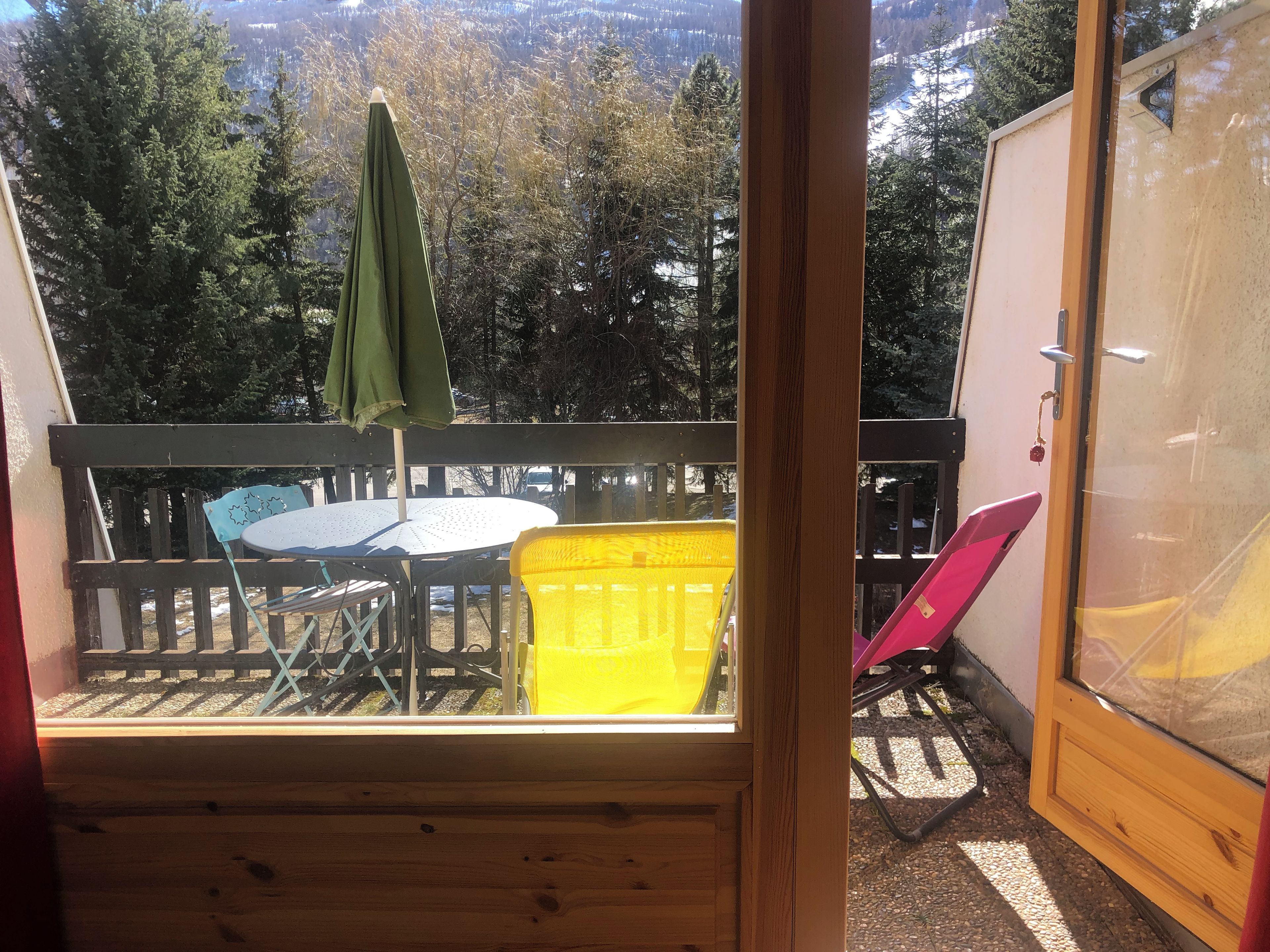 A wooden deck with a table and chairs, a yellow basket, and a green umbrella.