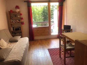 A room with a wooden floor, a sofa, a bookshelf, a table, and a TV. - Quaint 1-bedroom house in Saint-Chaffrey perfect for relaxing stays (Saint-Chaffrey)
