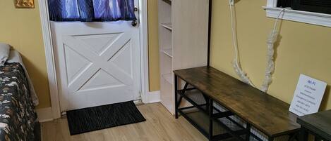 A room with a door, a small table, a bench, a radiator, and a power outlet.