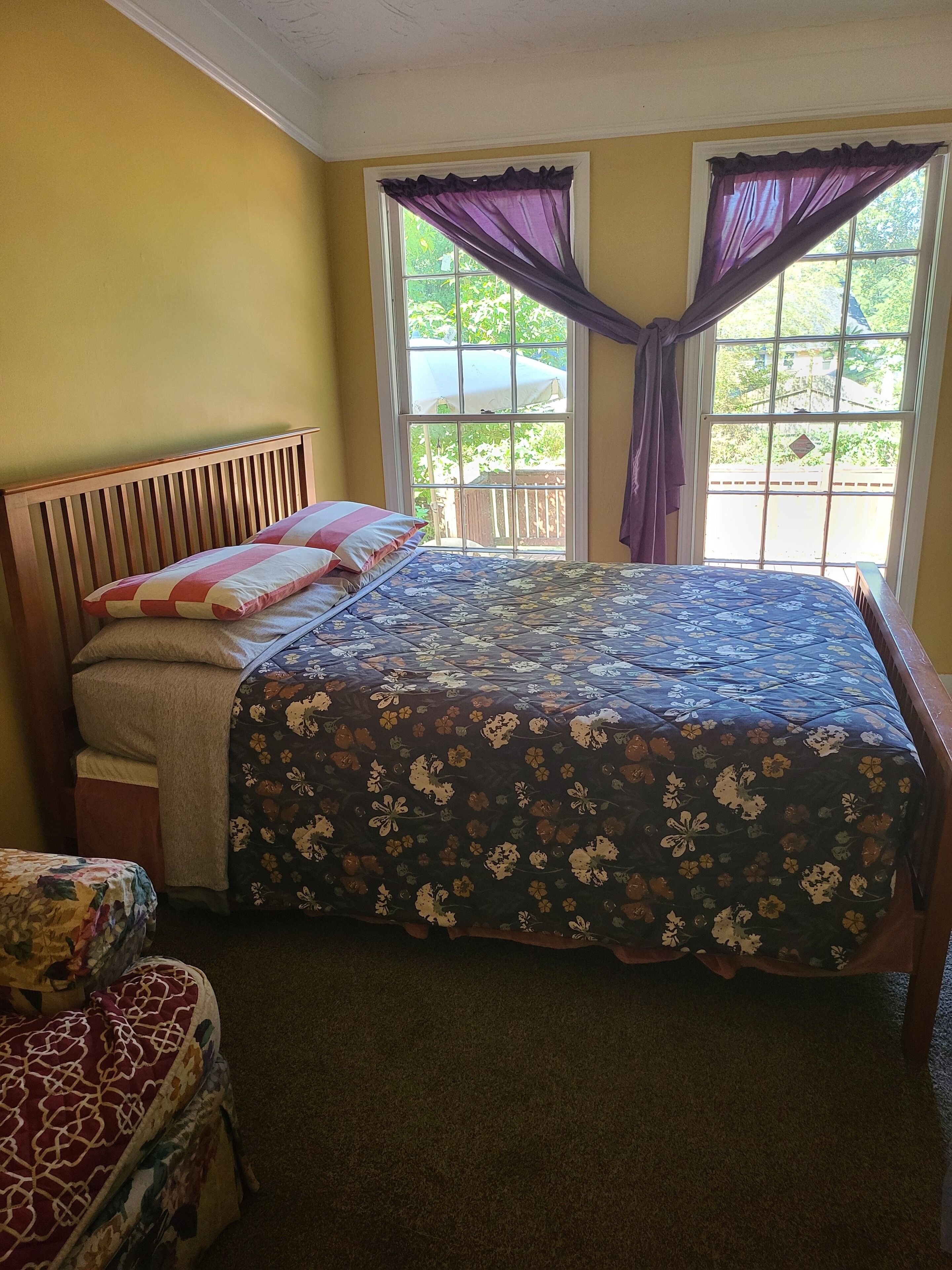 A bedroom with a bed, a wooden headboard, a window with curtains, and a view of greenery outside.