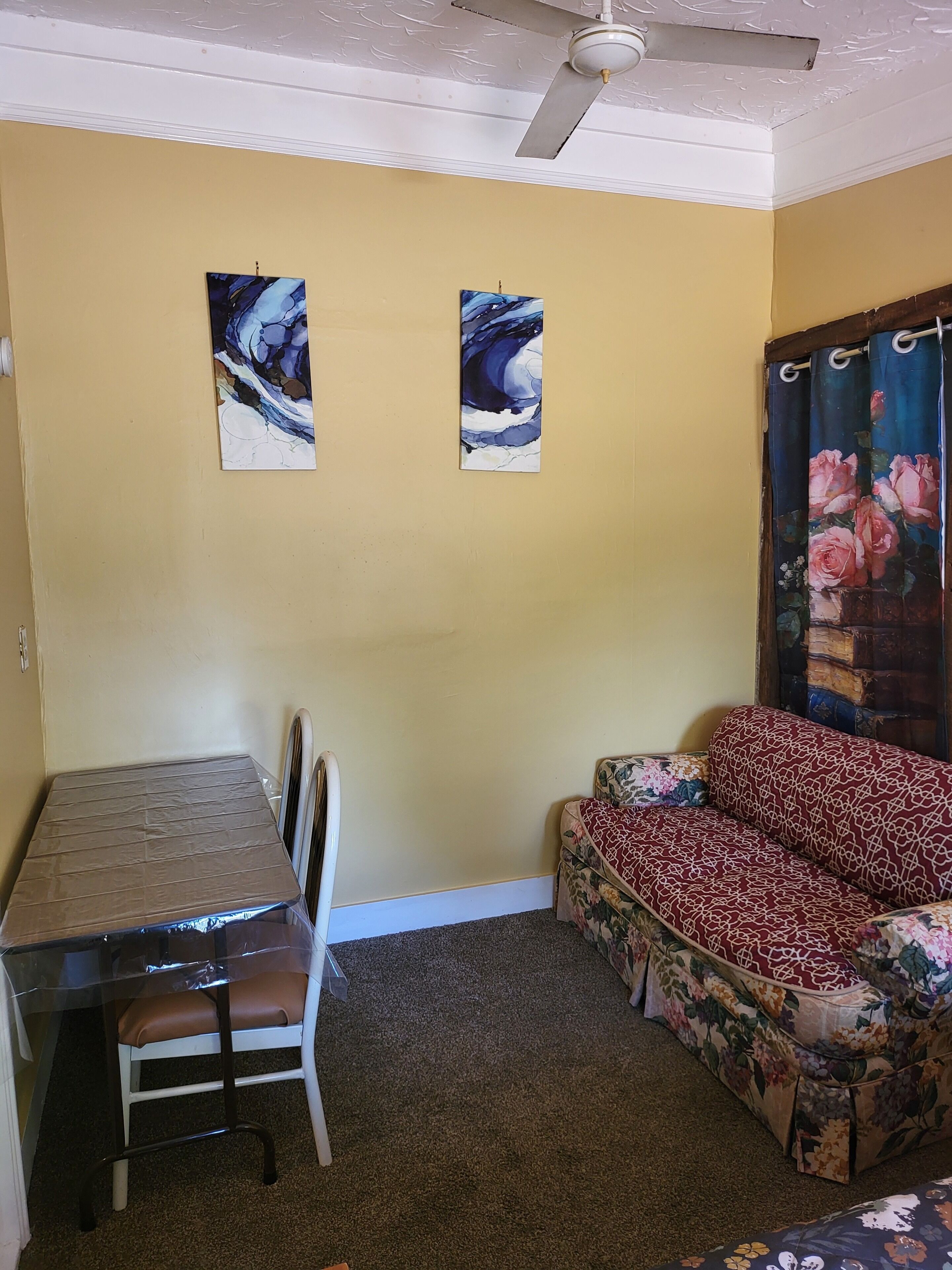 A room with a dining table, a sofa, and two wall-mounted paintings.