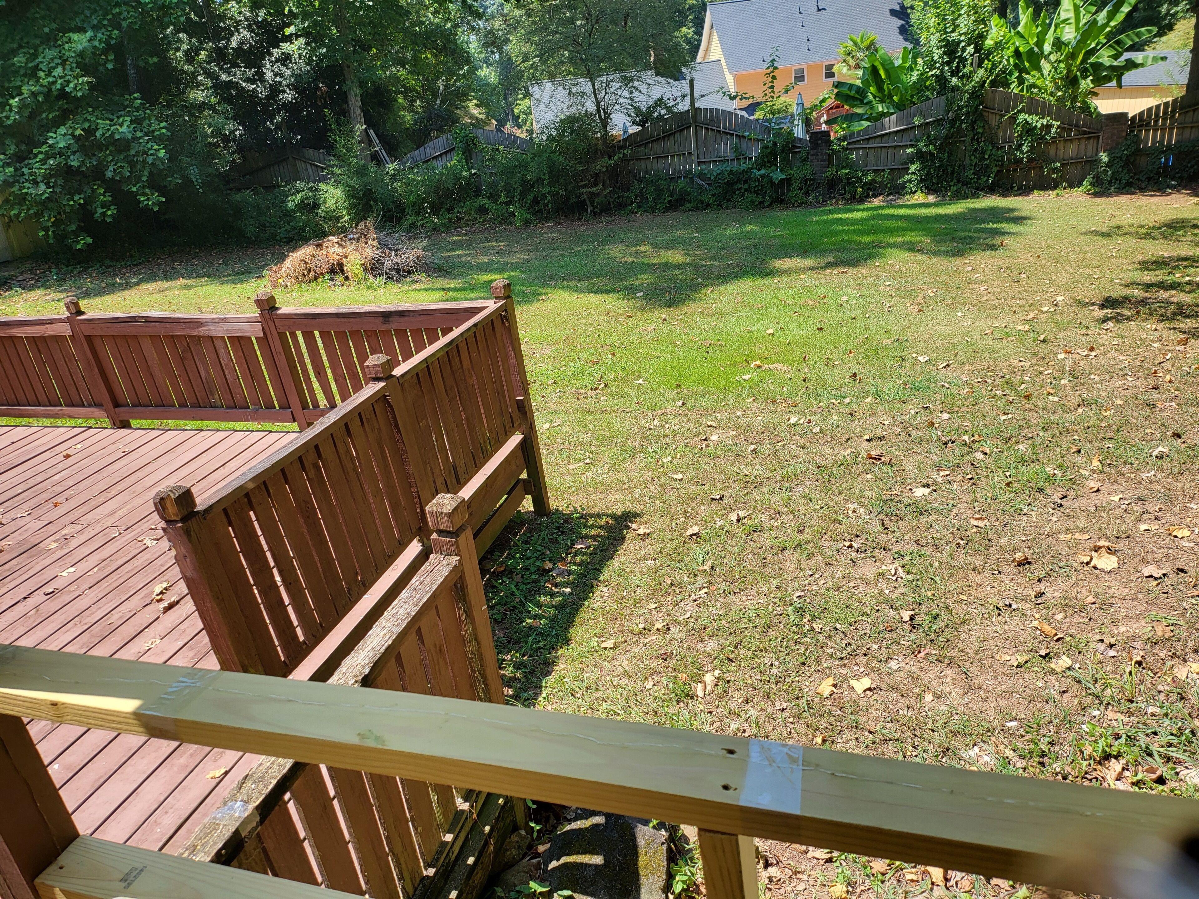 A wooden deck with a bench, surrounded by a grassy yard and a wooden fence.