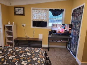 A bedroom with a bed, a desk with a computer, a window with curtains, and a bookshelf.