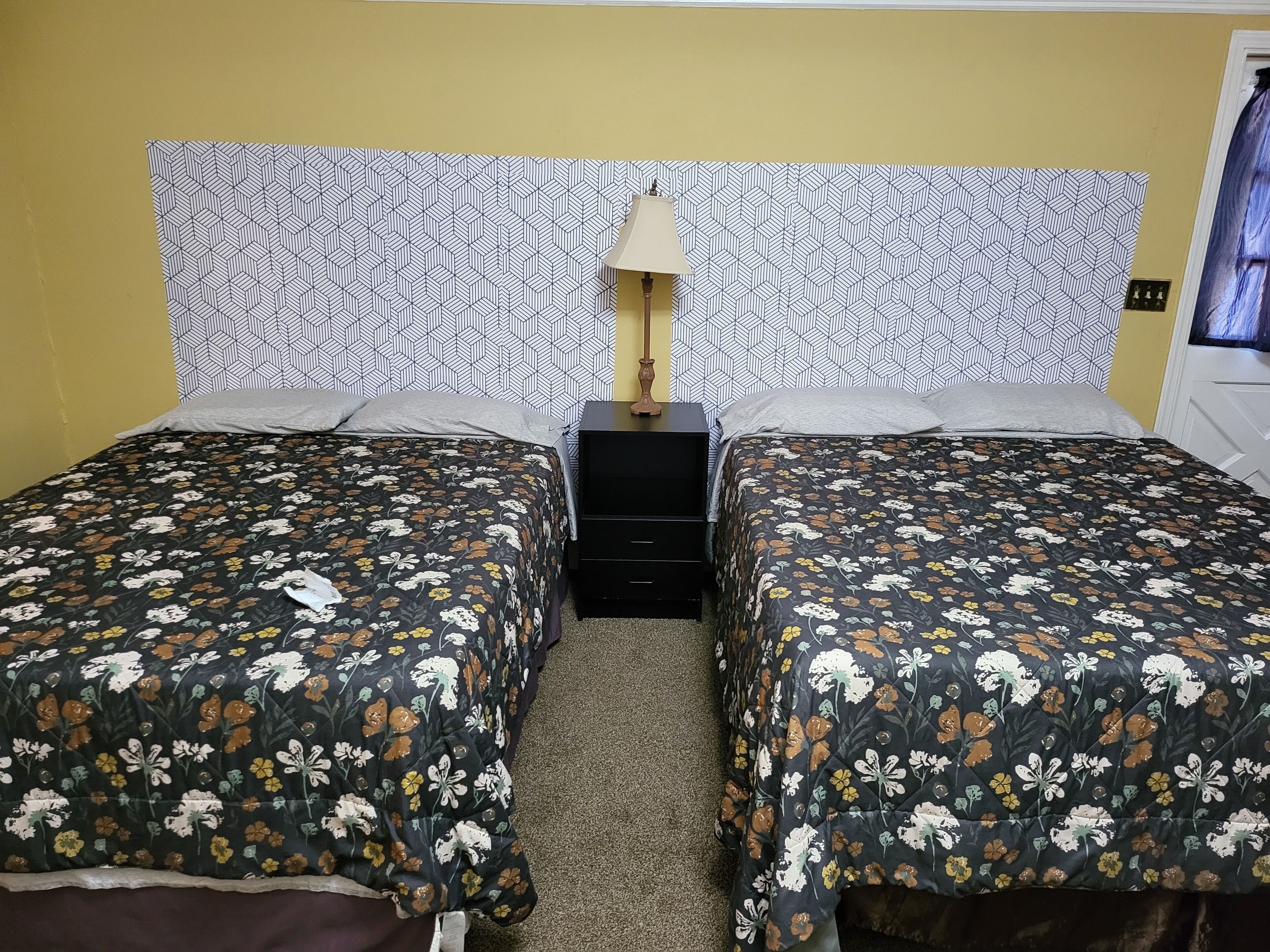 Un lit double avec une literie à motifs floraux, une table de chevet avec une lampe et une tête de lit décorée.