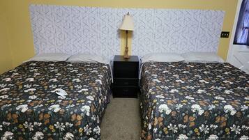Un lit double avec une literie à motifs floraux, une table de chevet avec une lampe et une tête de lit décorée.