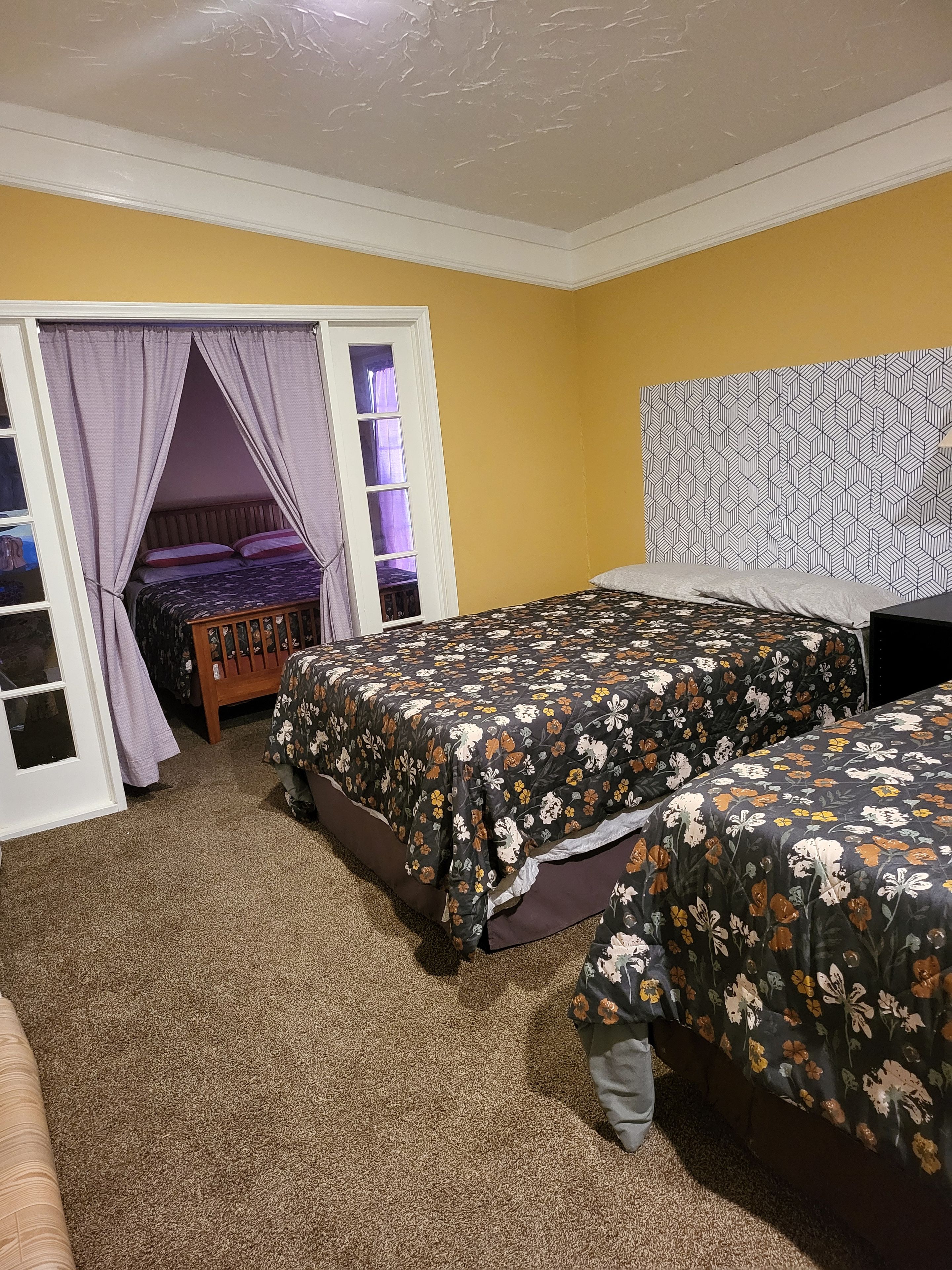 A bedroom with two beds, a window with curtains, and a patterned wall.