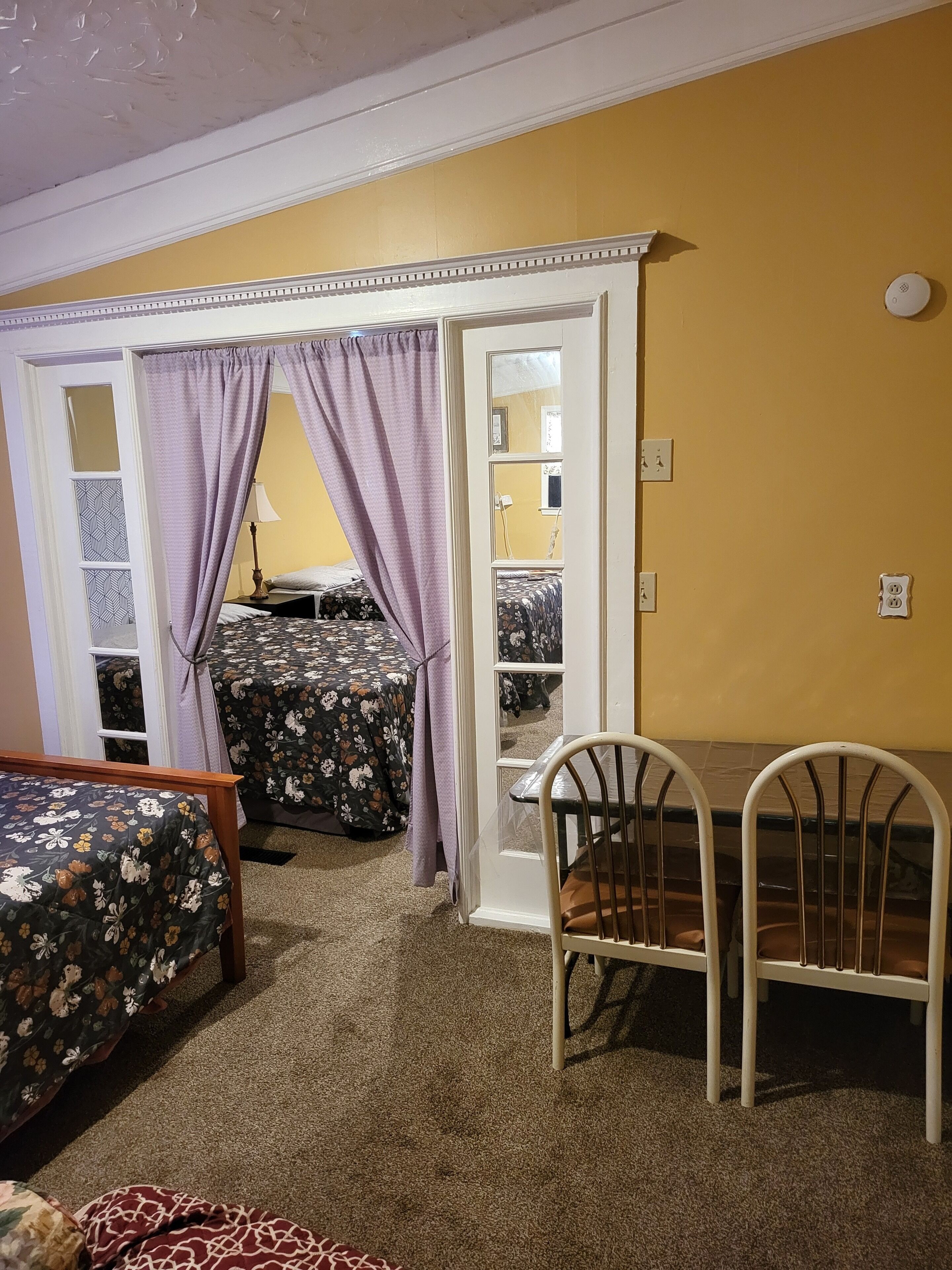 A room with a bed, a table with chairs, a door, and a mirror.