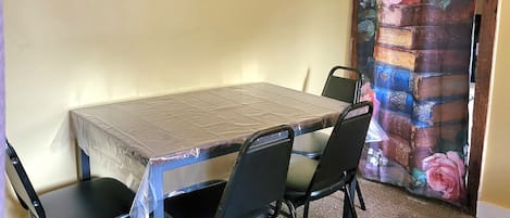 A dining area with a table and chairs, a wall with two paintings, and a curtain with a floral pattern.