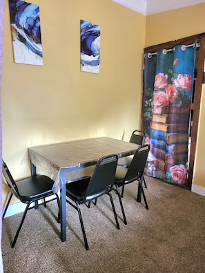 A dining area with a table and chairs, a wall with two paintings, and a curtain with a floral pattern.