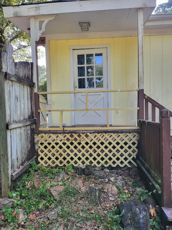 A wooden porch with a yellow door and a lattice railing.