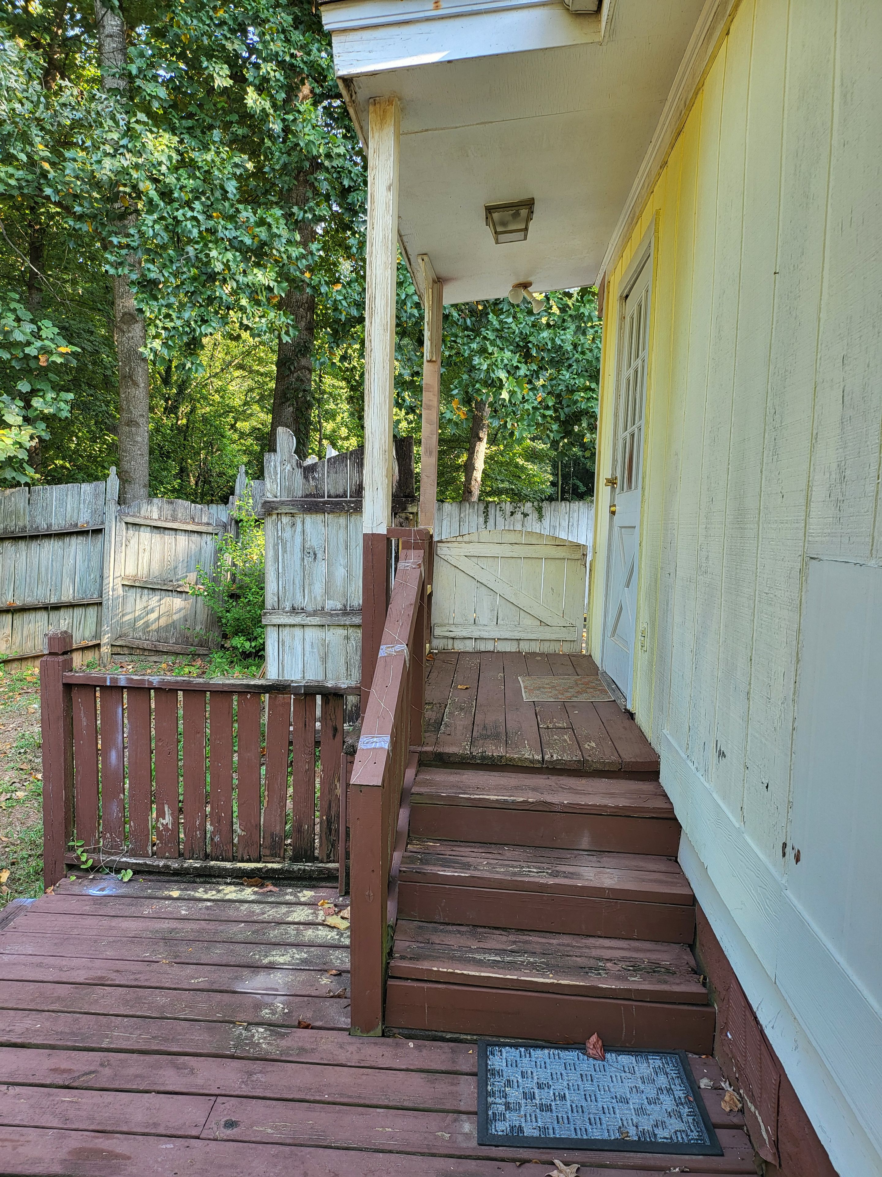 Un escalier en bois mène à un porche doté d’un paillasson en métal.