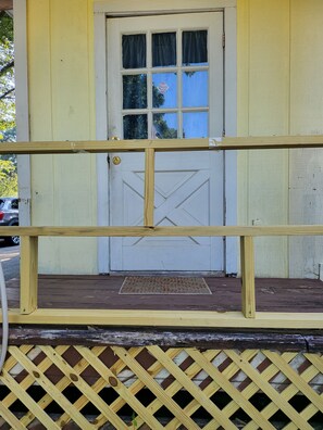 A wooden porch with a lattice railing, a white door with a window, and a doormat.