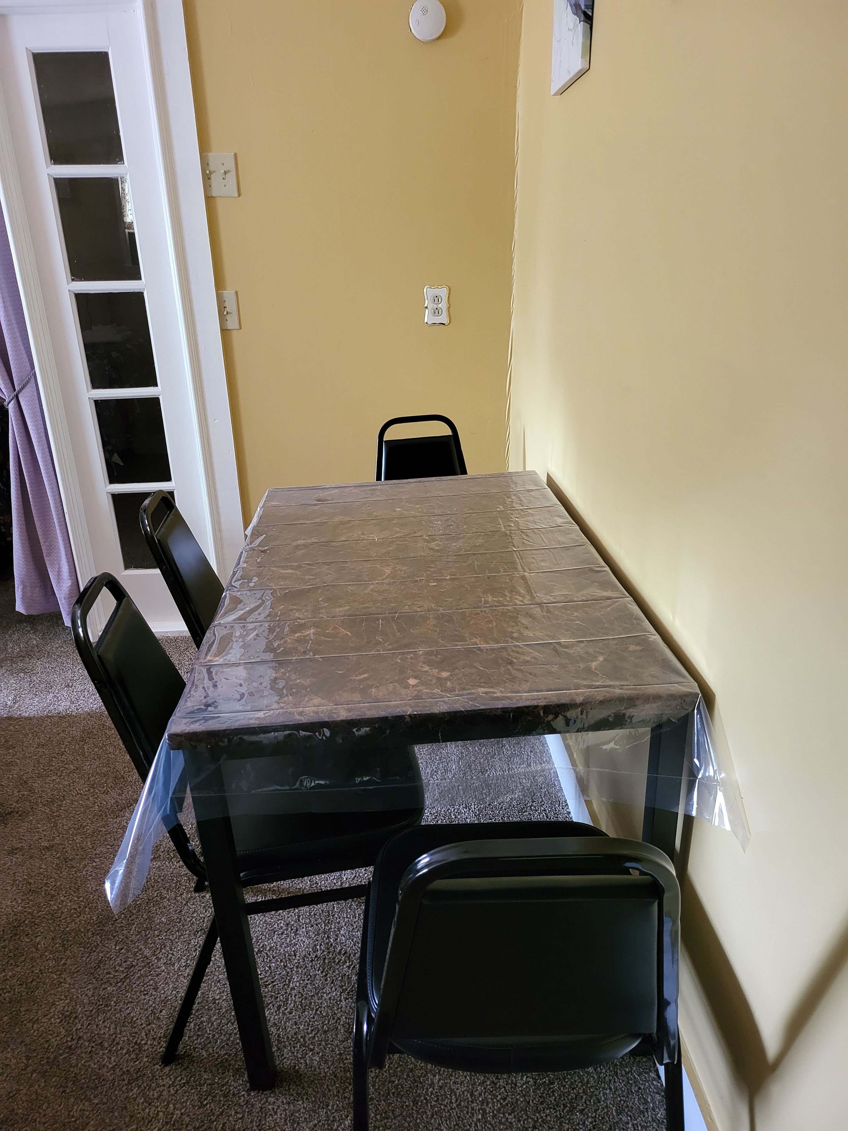 A room with a large table, two chairs, a door, and a light switch on the wall.