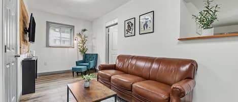 Una sala de estar con un sofá de cuero marrón, un sillón azul, una mesa de centro de madera y una lámpara de pie.