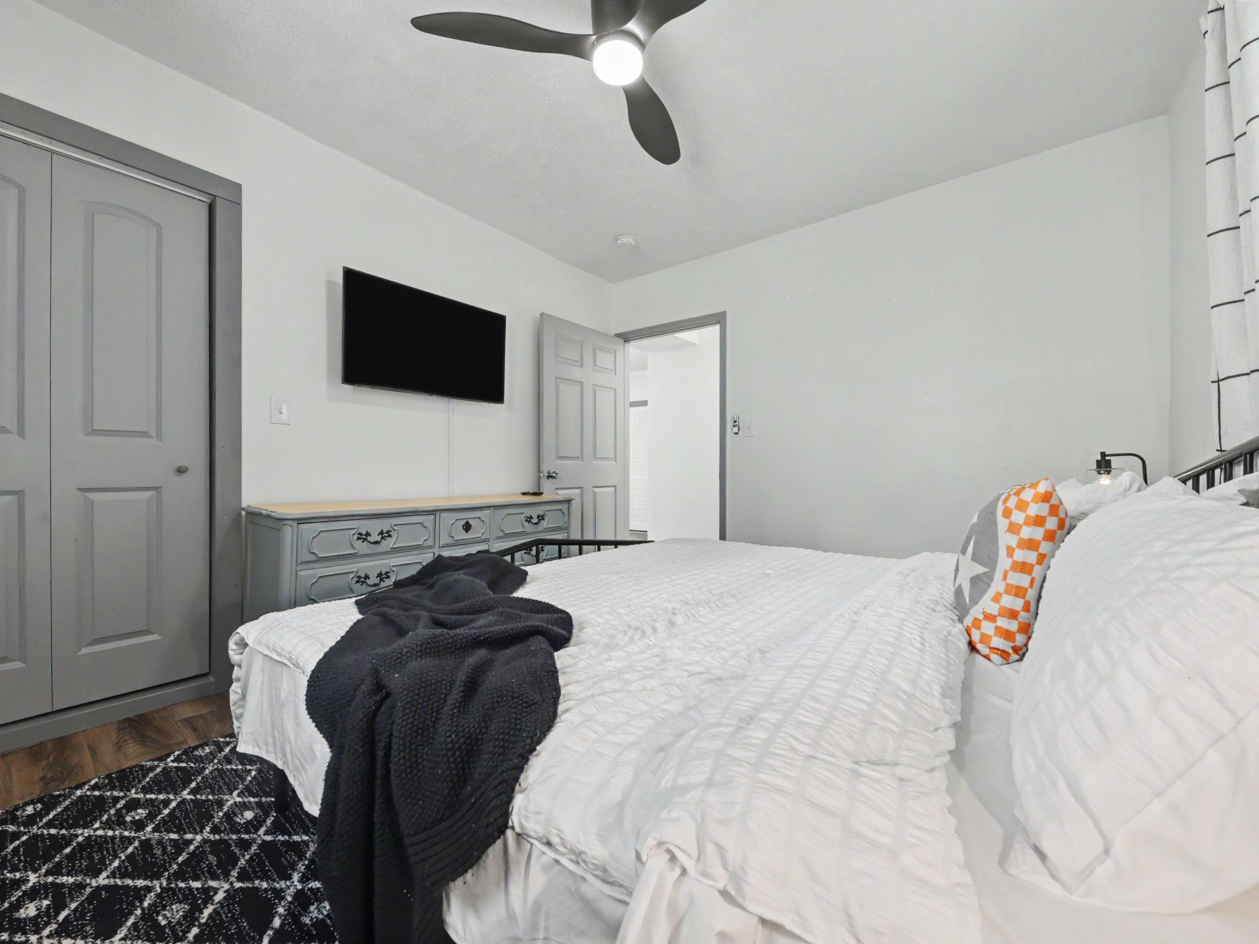A bedroom with a bed, a ceiling fan, a dresser, and a television.